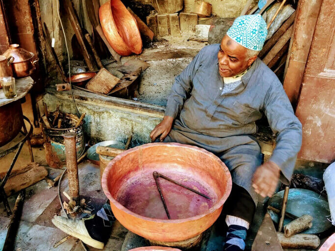 ein älterer marokkanischer Handwerker bearbeitet seine Kupfertöpfe in seiner Straßenwerkstatt